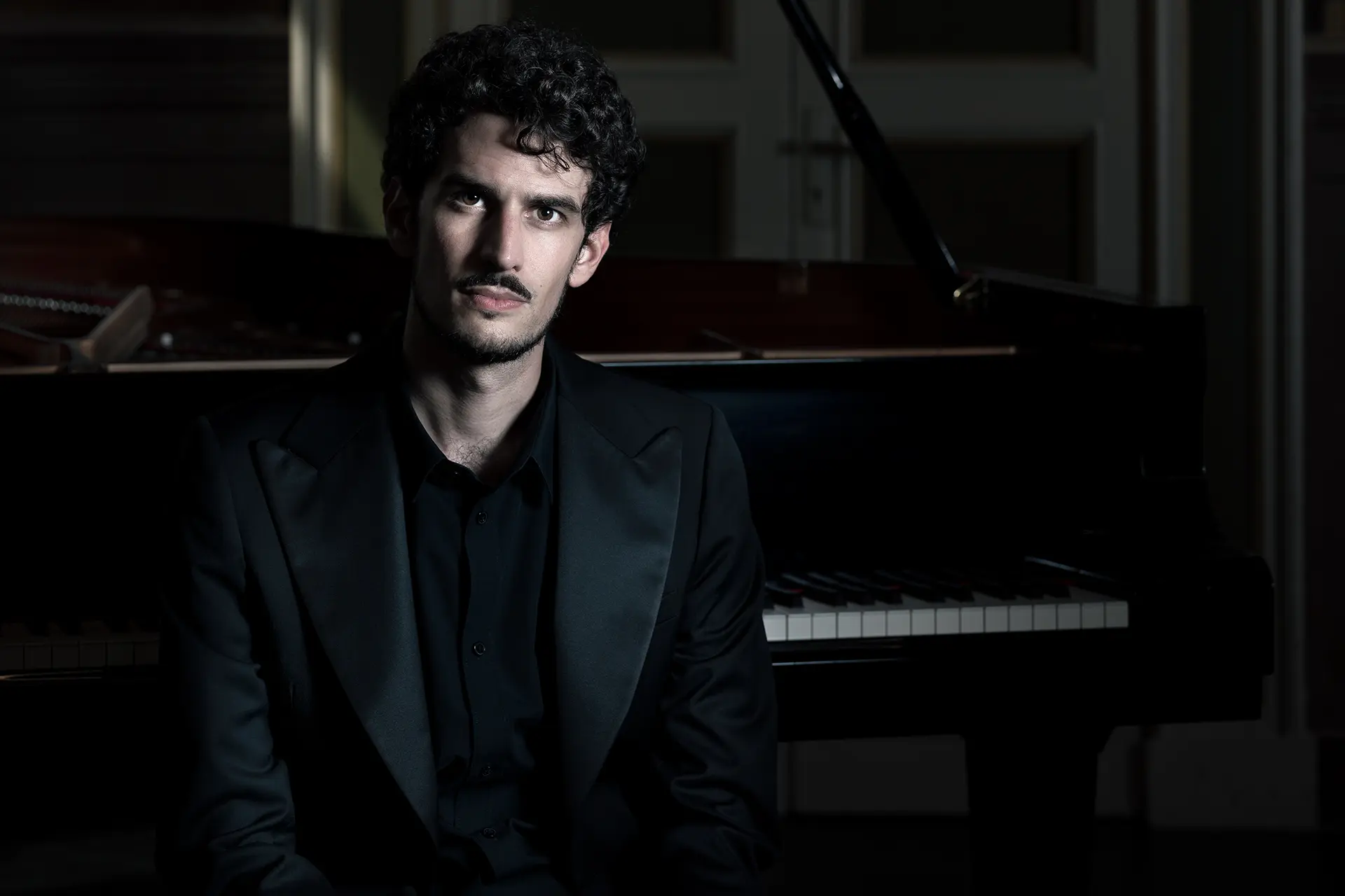 Federico Ercoli, a pianist and musicologist, is in front of a grand piano, elegant and serious.